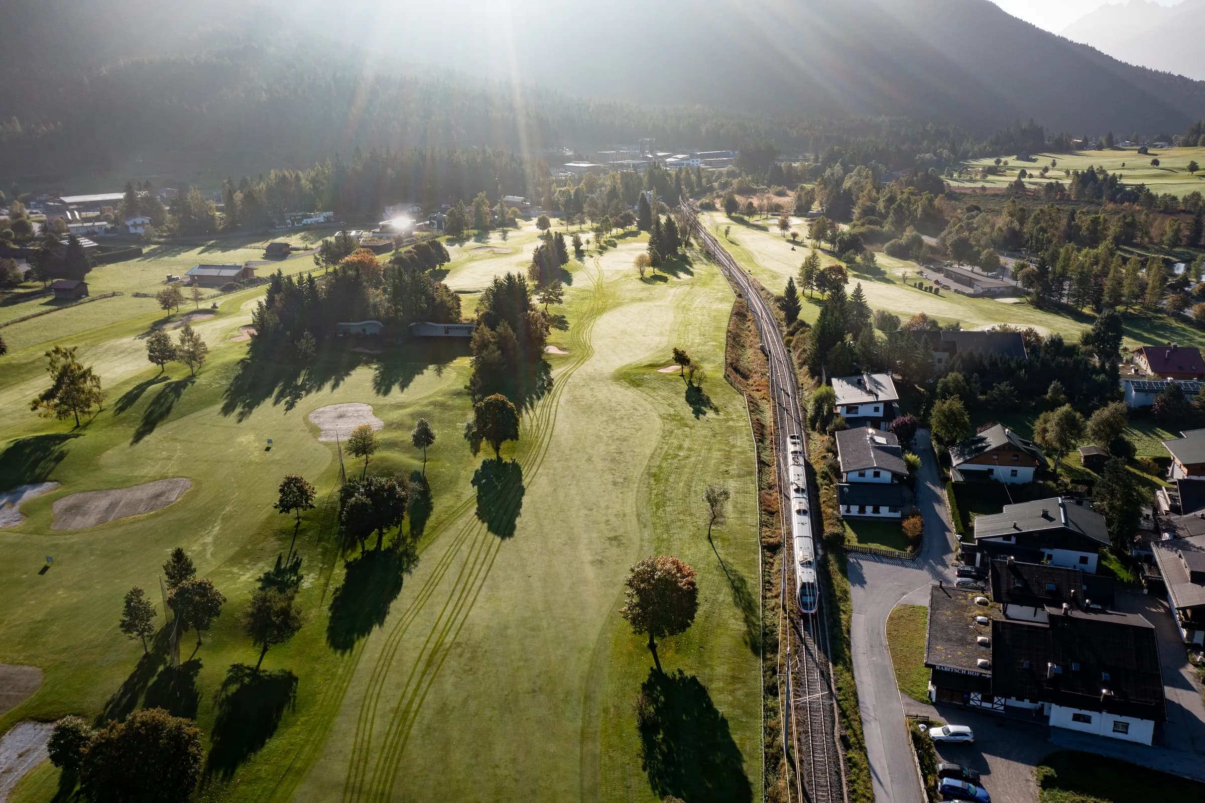 Drohnenaufnahme über dem Golfplatz Seefeld mit Blick auf die Bahnstrecke und einen vorbeifahrenden Zug