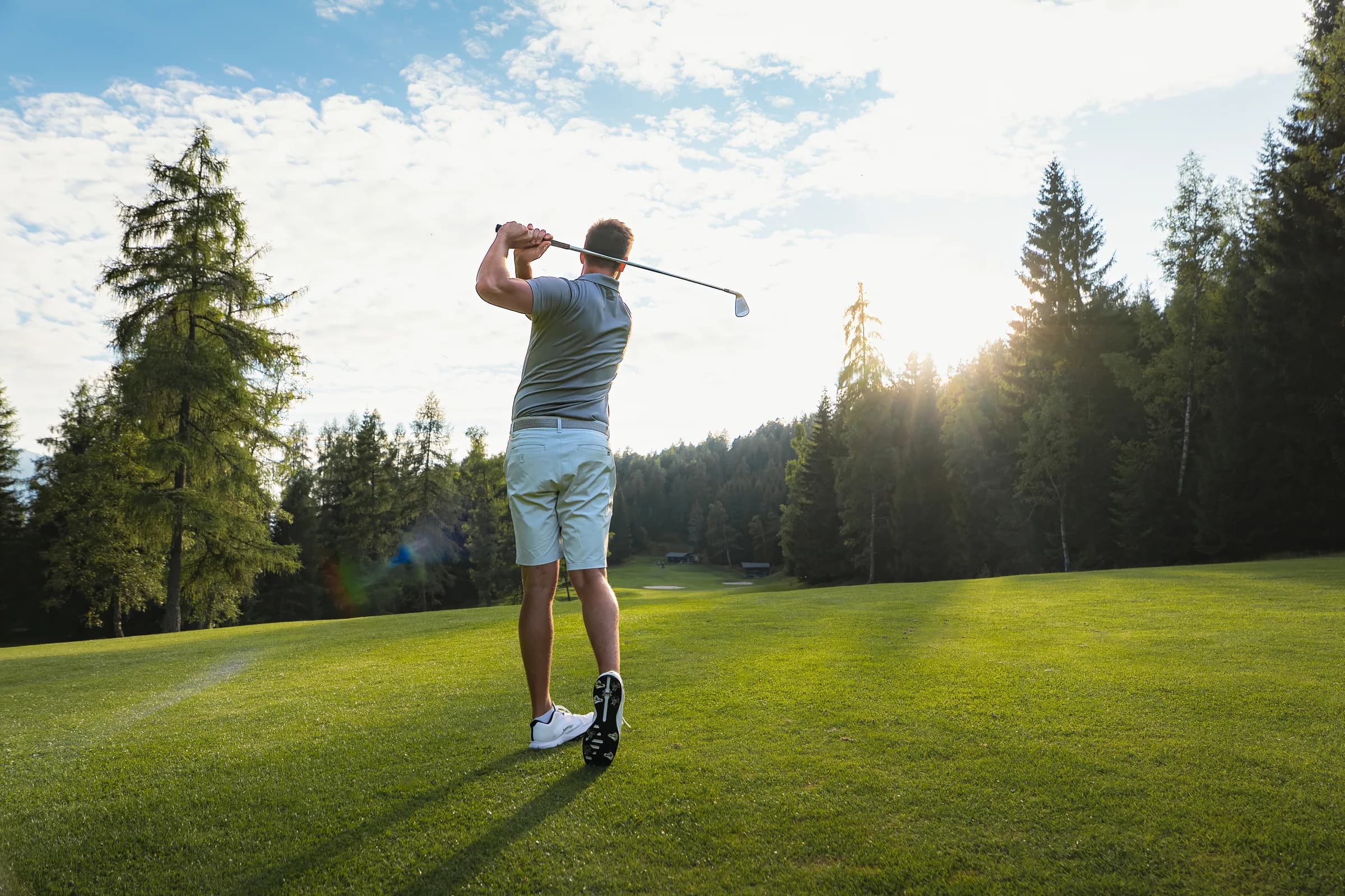 Ein Golfer beim Abschlag im Golfclub Wildmoos bei Sonnenuntergang, von hinten fotografiert